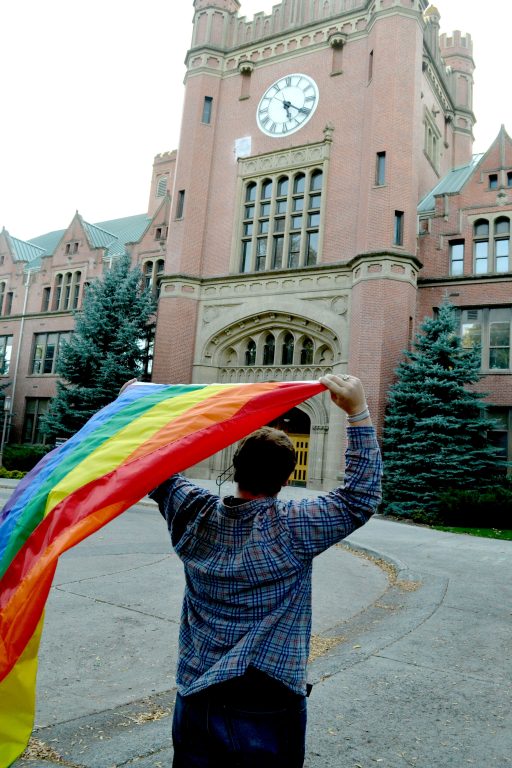 Hagen holding the Pride Flag in front of the Admin building on campus
